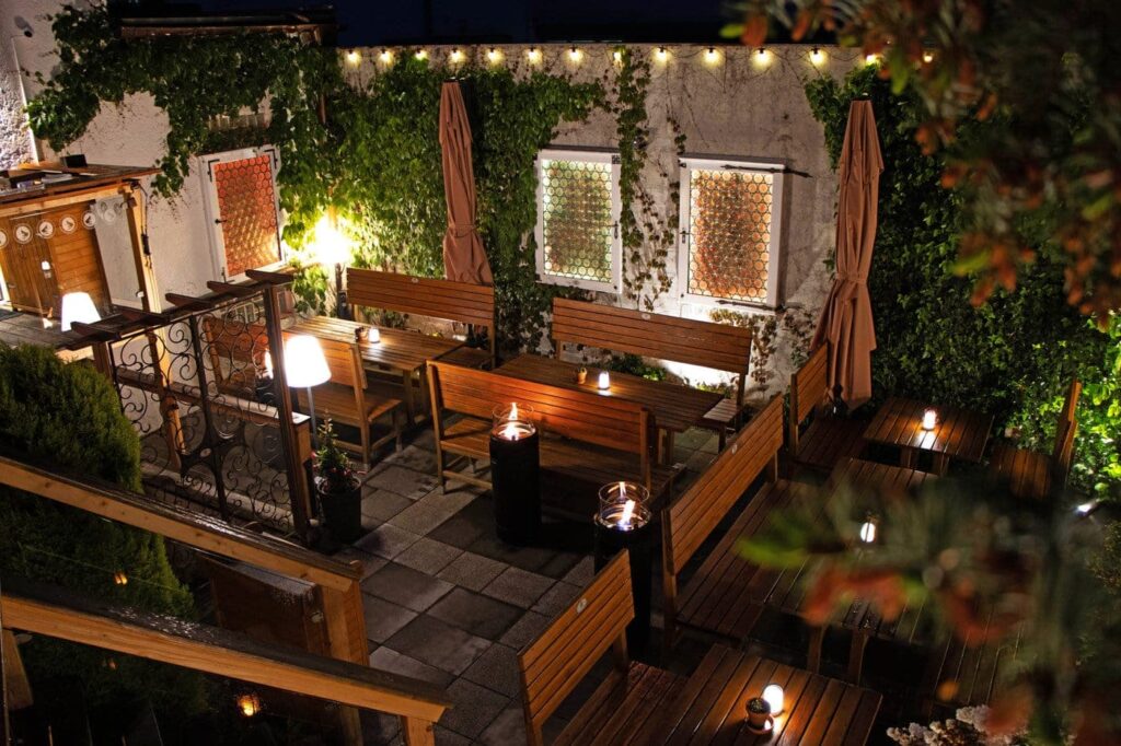 Blick zum schön beleuchteten Biergarten des Atelier Teufelsbäck am Abend.